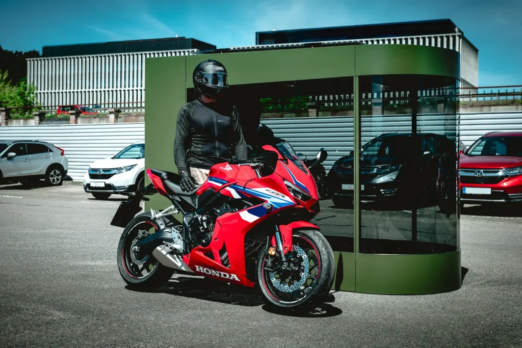 Motorcyclist in riding gear standing next to a MotoDome garage outdoors